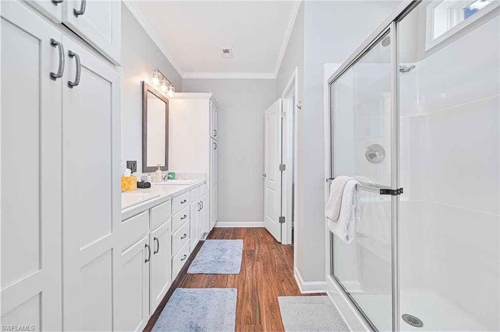 Full bathroom featuring ornamental molding, double vanity, a stall shower, and dark wood-type flooring