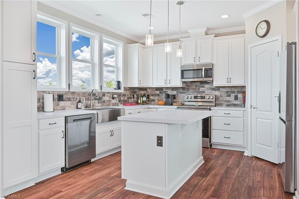 Kitchen with light countertops, appliances with stainless steel finishes, white cabinetry, crown molding, and decorative light fixtures