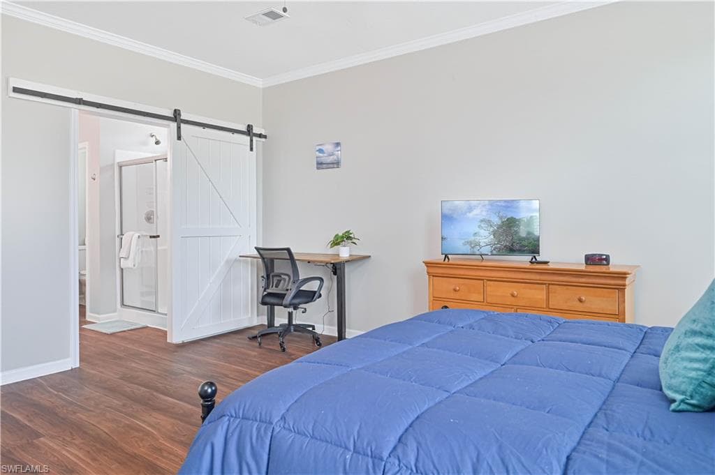 Bedroom featuring dark wood-style floors, crown molding, and a barn door