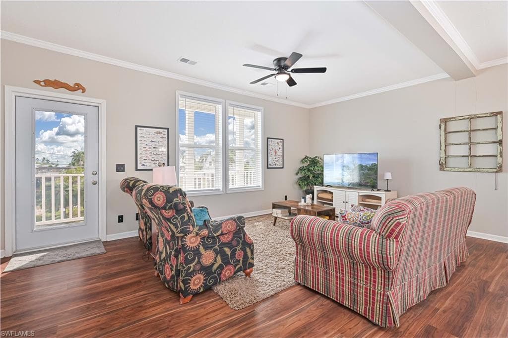 Living room with crown molding, dark wood-type flooring, and a ceiling fan