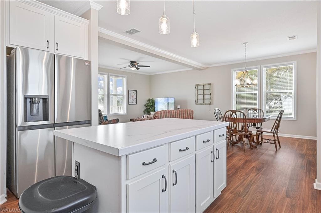 Kitchen featuring stainless steel fridge with ice dispenser, white cabinets, decorative light fixtures, crown molding, and light countertops