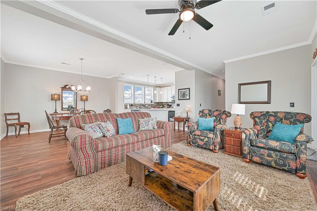 Living room featuring a chandelier, ornamental molding, wood finished floors, and a ceiling fan
