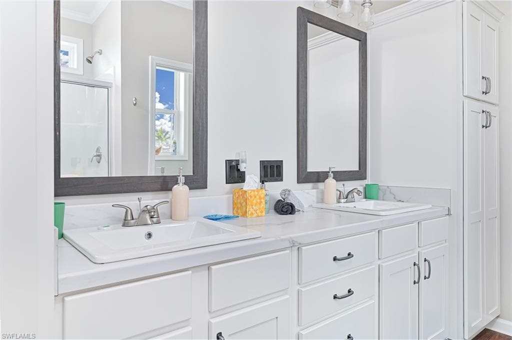 Bathroom featuring plenty of natural light, a stall shower, crown molding, and double vanity