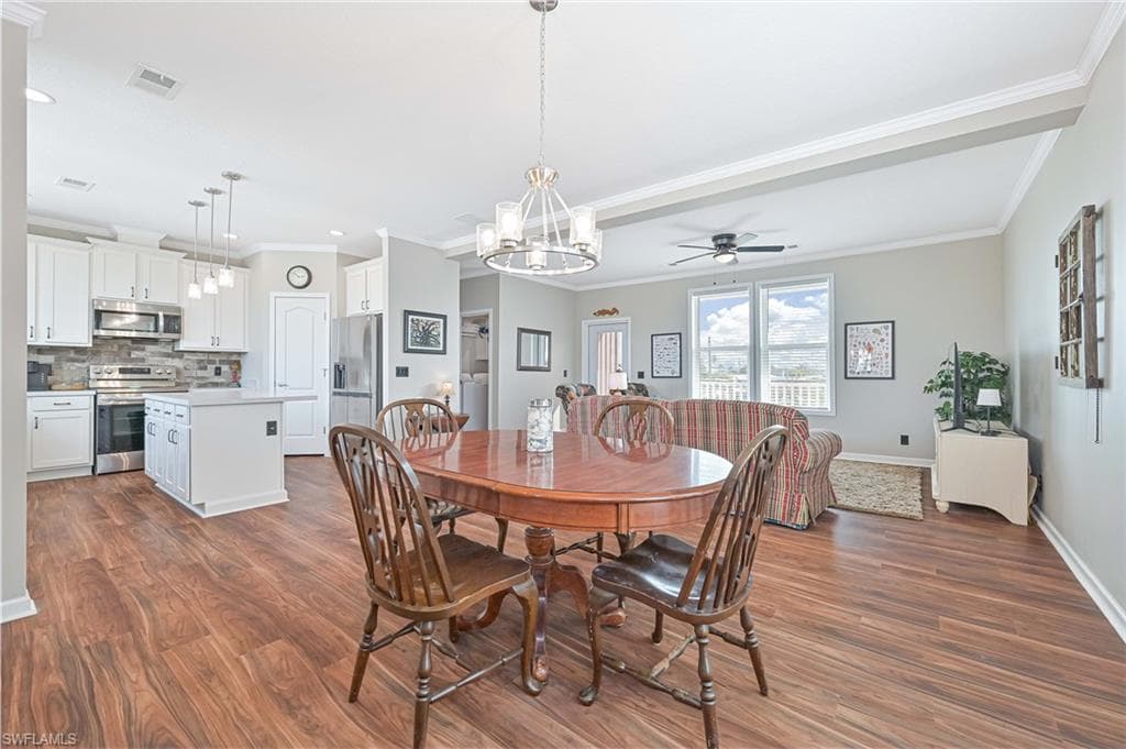 Dining room featuring a chandelier, a ceiling fan, crown molding, and dark wood-style flooring