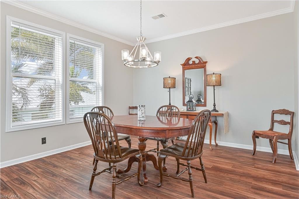 Dining room with dark wood-type flooring, crown molding, and a chandelier