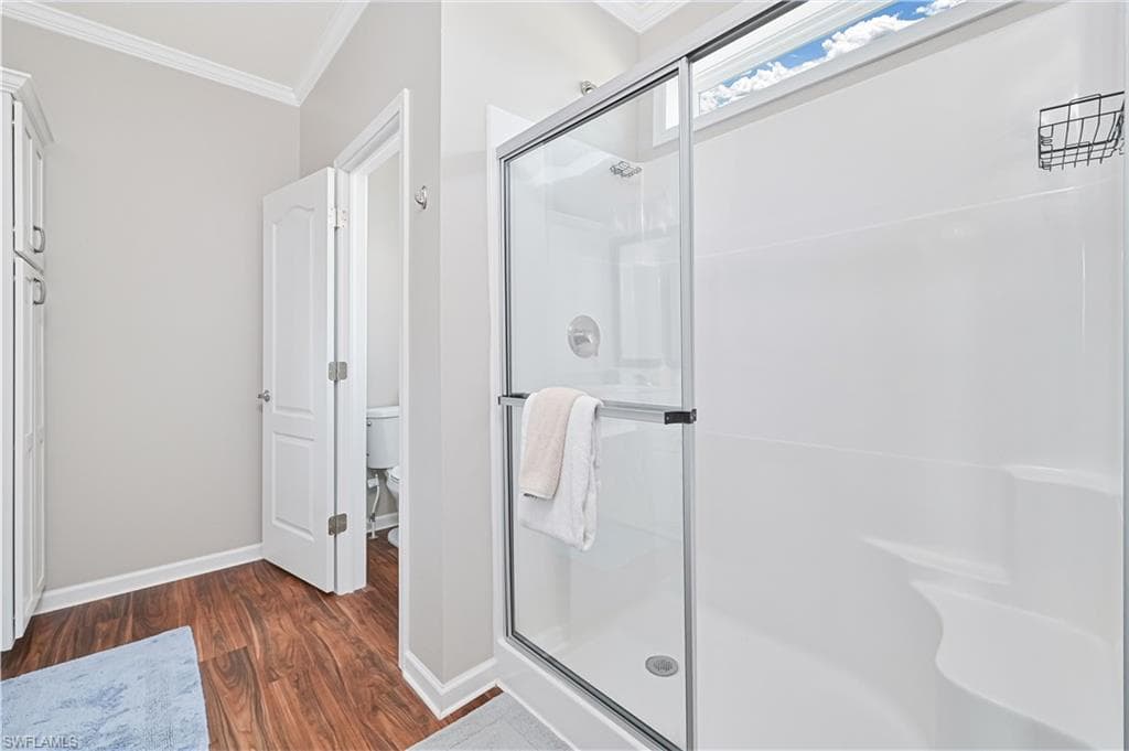 Full bath featuring ornamental molding, dark wood-style flooring, and a stall shower
