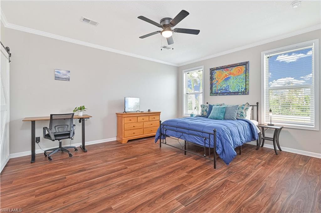 Bedroom with ornamental molding, wood finished floors, a ceiling fan, a desk, and a barn door