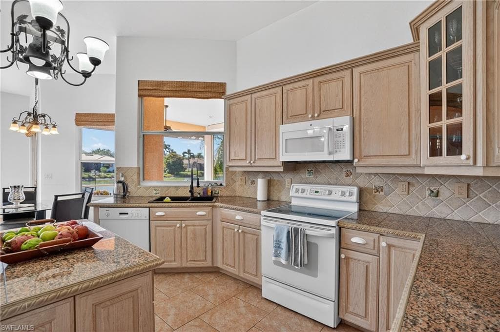 Kitchen with white appliances, light brown cabinets, decorative backsplash, a chandelier, and glass insert cabinets