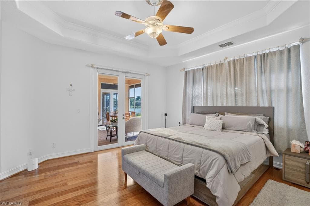 Bedroom featuring access to exterior, hardwood / wood-style floors, crown molding, ceiling fan, and a raised ceiling