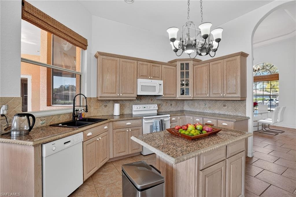 Kitchen featuring white appliances, light brown cabinetry, glass insert cabinets, pendant lighting, and light tile patterned flooring