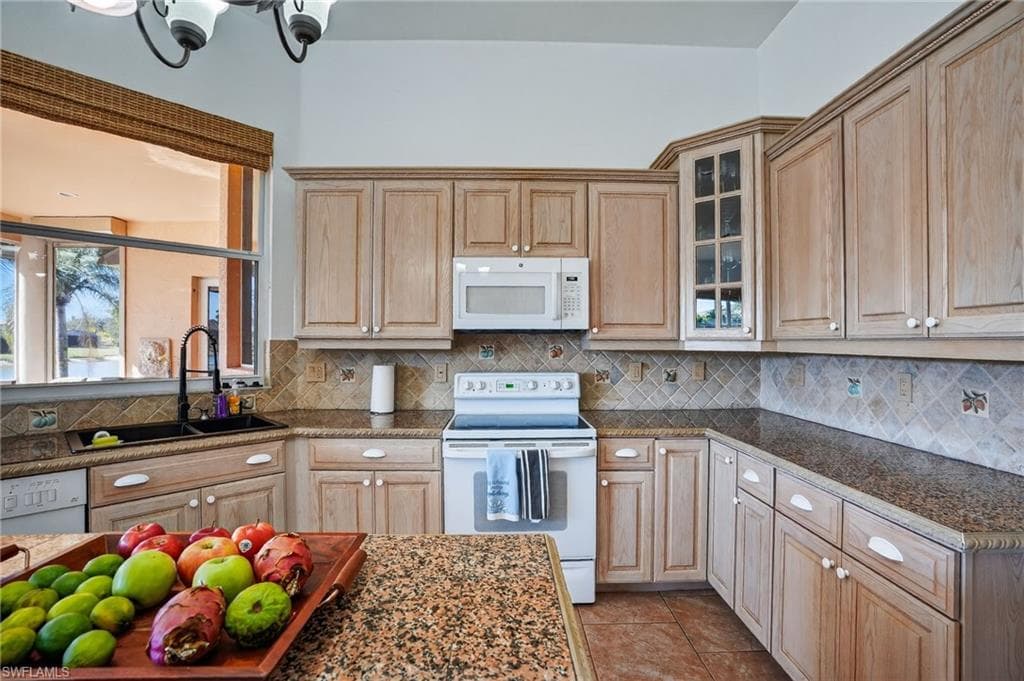 Kitchen featuring white appliances, light tile patterned floors, glass insert cabinets, and light brown cabinetry