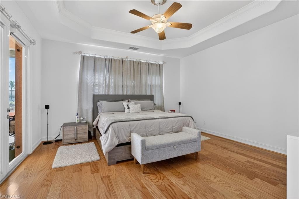 Bedroom with access to exterior, crown molding, wood finished floors, a ceiling fan, and a tray ceiling