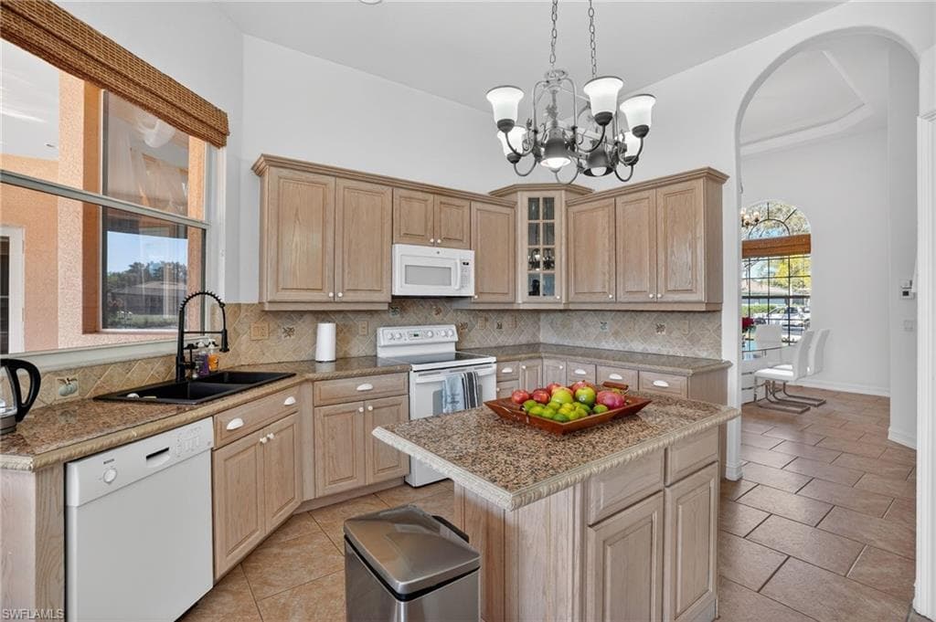 Kitchen with light brown cabinets, white appliances, glass insert cabinets, light tile patterned flooring, and hanging light fixtures