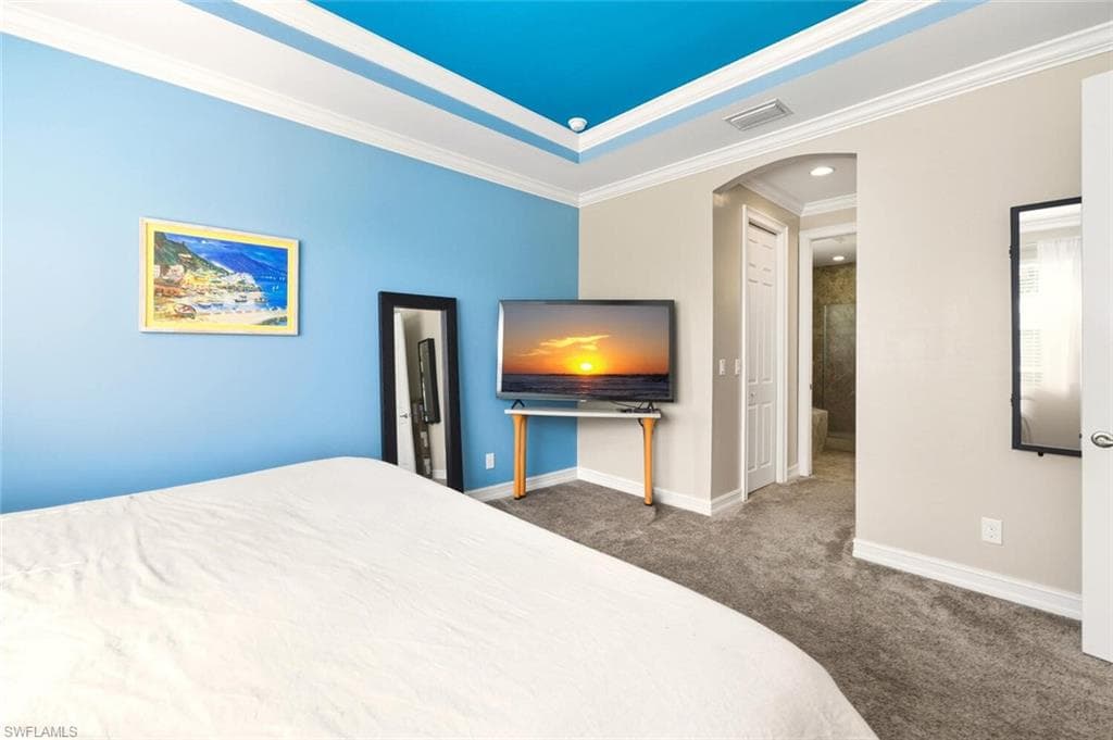 Carpeted bedroom with arched walkways, a closet, ornamental molding, and a raised ceiling