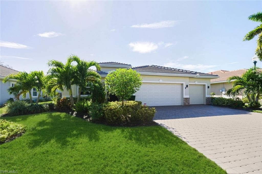 View of front of house with a front yard, decorative driveway, a garage, stucco siding, and stone siding