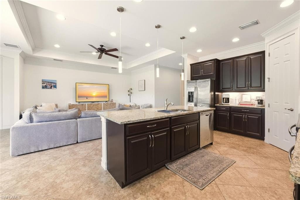 Kitchen with dark brown cabinetry, crown molding, a raised ceiling, decorative light fixtures, and light stone countertops