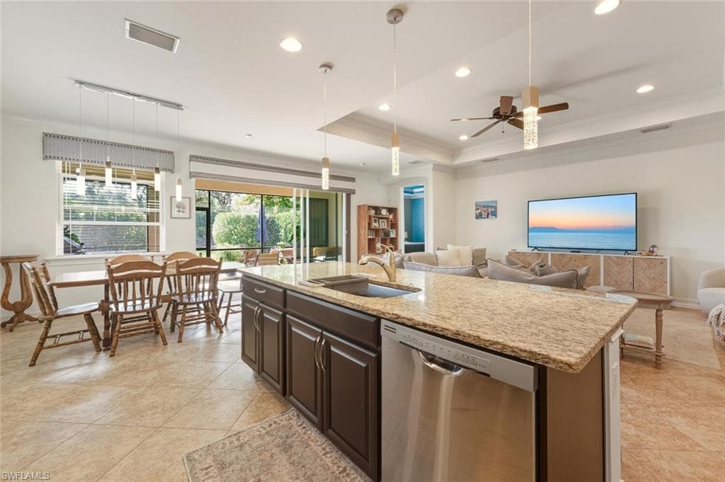 Kitchen featuring crown molding, stainless steel dishwasher, dark brown cabinets, pendant lighting, and an island with sink
