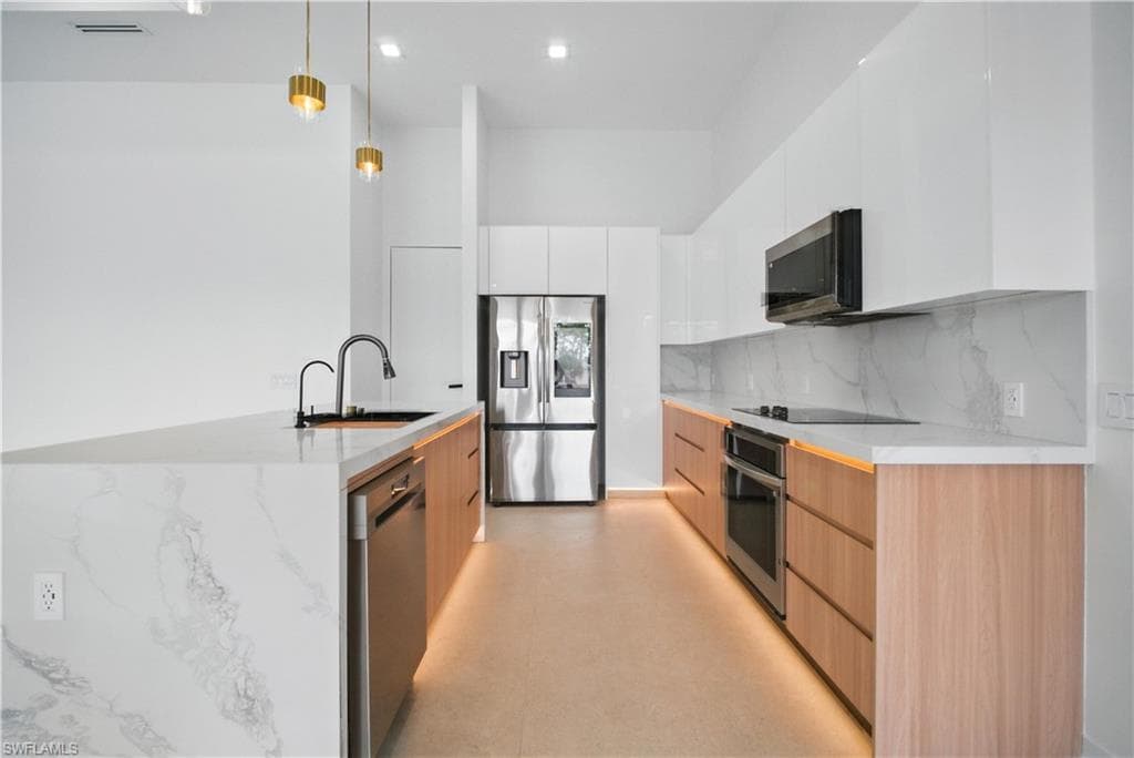 Kitchen featuring modern cabinets, hanging light fixtures, white cabinets, appliances with stainless steel finishes, and backsplash