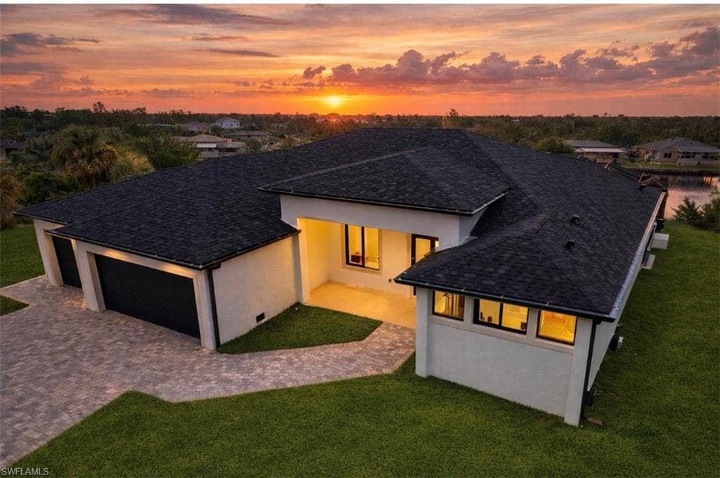 Back of house featuring stucco siding, a lawn, decorative driveway, and roof with shingles (Rendered photo)