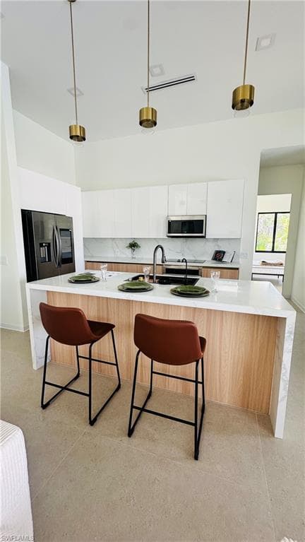 Modern kitchen featuring a large waterfall island with wood-finish paneling, white countertops, and a black stainless steel refrigerator