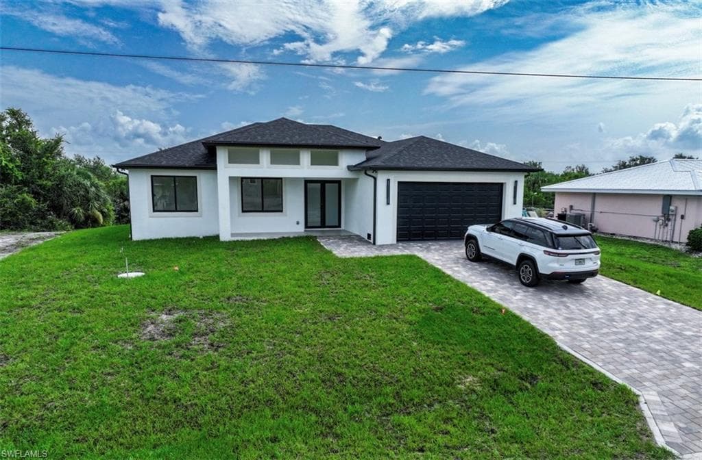 Prairie-style home featuring a front yard, stucco siding, decorative driveway, and an attached garage