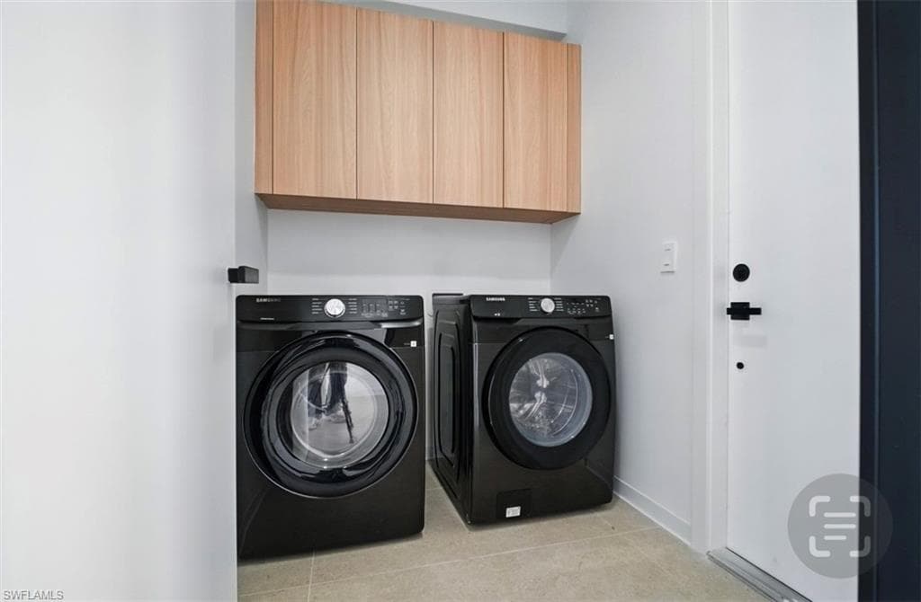 Laundry area featuring washer and clothes dryer, cabinet space, and light tile patterned floors