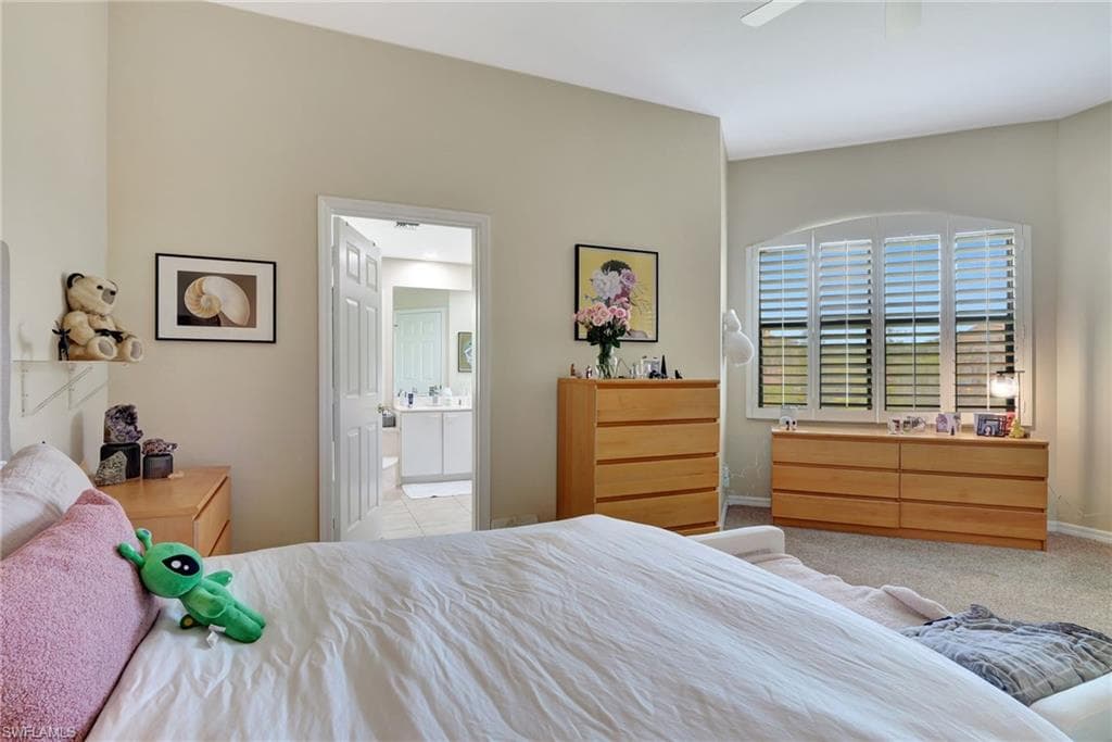 Carpeted bedroom with ceiling fan, connected bathroom, and baseboards