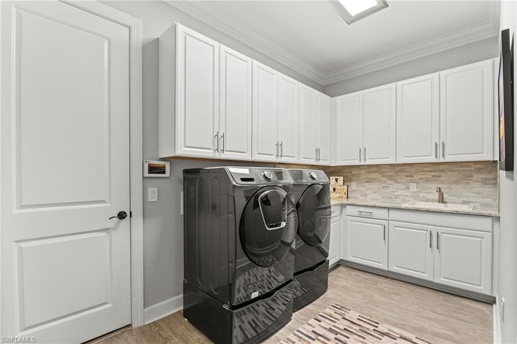 Laundry room featuring crown molding, separate washer and dryer, light wood-style floors, and cabinet space