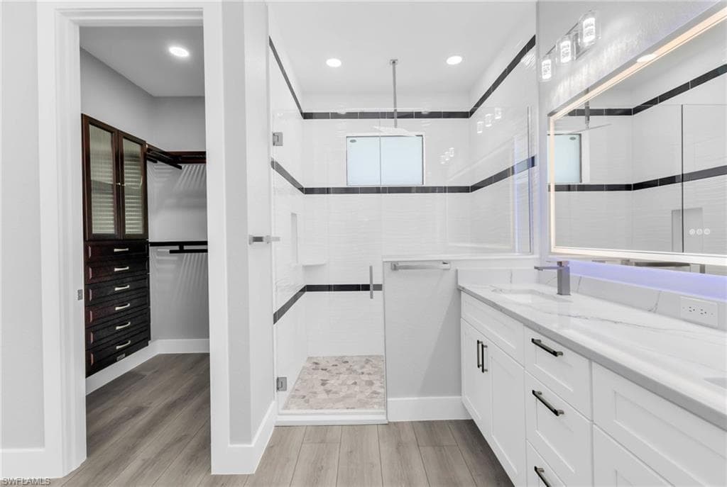 Full bathroom with a walk in closet, double vanity, a shower stall, light wood finished floors, and recessed lighting