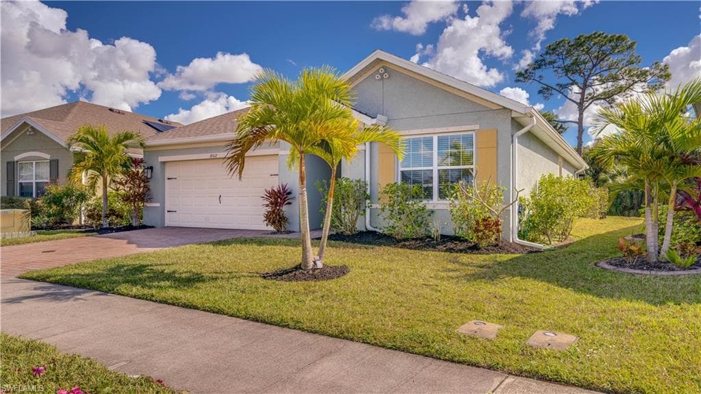 Ranch-style house featuring stucco siding, a front yard, driveway, and an attached garage