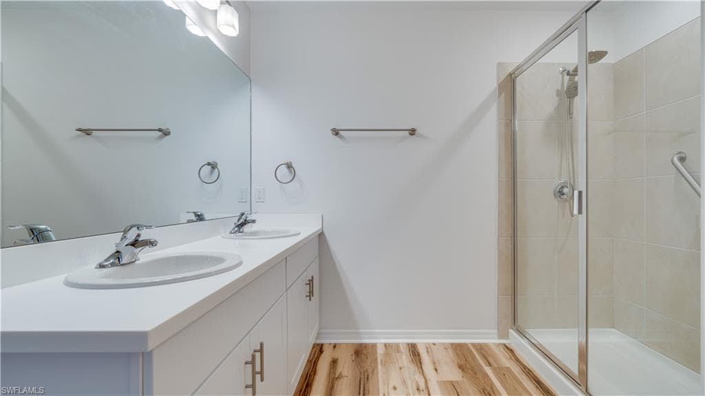 Bathroom with double vanity, a stall shower, and light wood finished floors