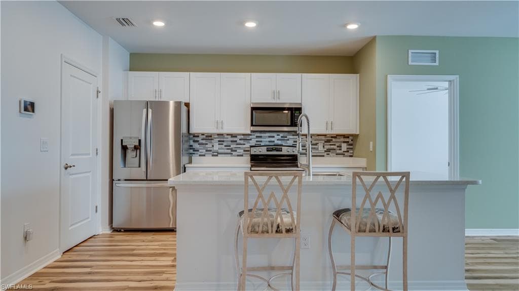 Kitchen with appliances with stainless steel finishes, white cabinetry, light stone counters, and an island with sink