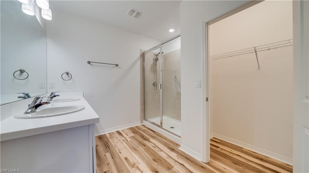 Full bath featuring double vanity, a shower stall, a walk in closet, light wood finished floors, and recessed lighting