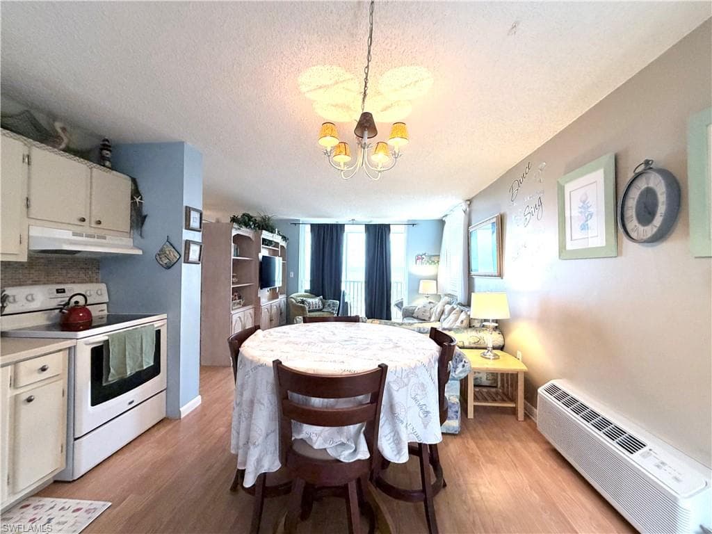 Kitchen featuring white electric range, light countertops, a textured ceiling, a wall mounted air conditioner, and under cabinet range hood