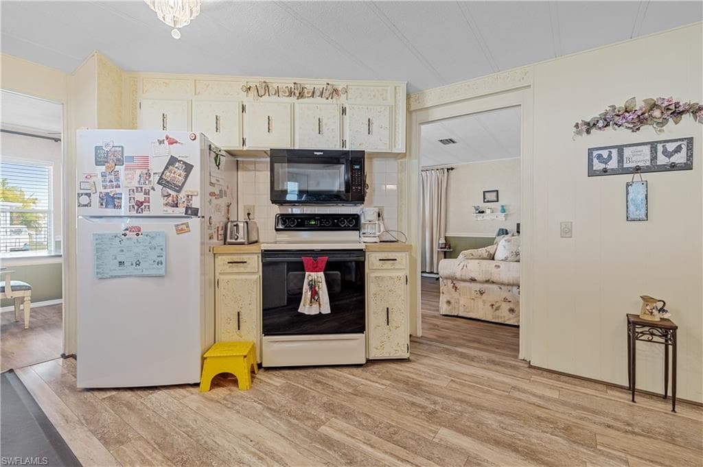 Kitchen featuring range with electric cooktop, freestanding refrigerator, black microwave, light countertops, and light wood-style floors