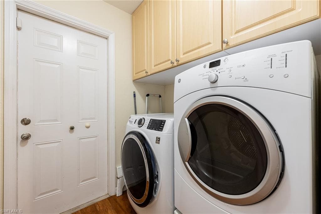 Washroom featuring washer and clothes dryer, dark wood-style floors, and cabinet space