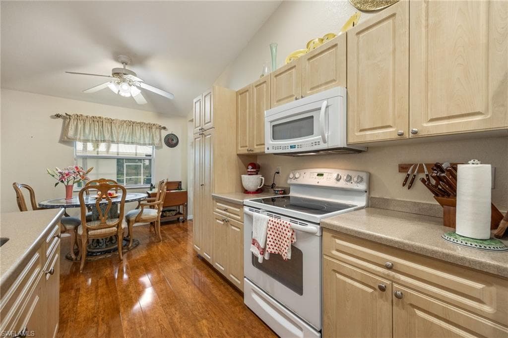 Kitchen featuring white appliances, light countertops, dark wood-style flooring, light brown cabinetry, and ceiling fan