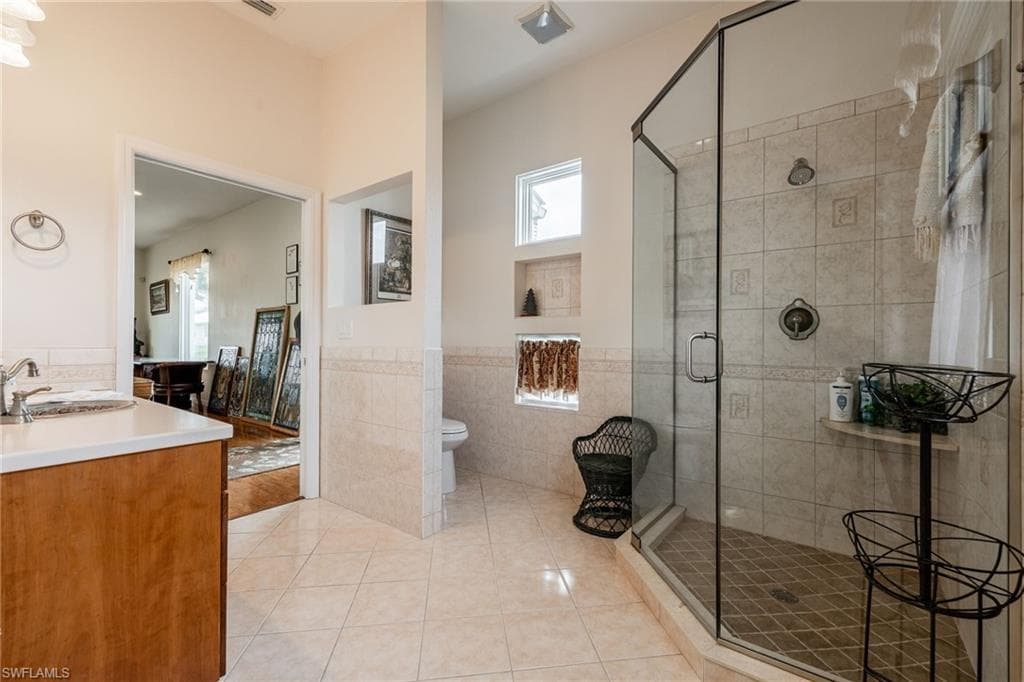 Bathroom featuring vanity, light tile patterned flooring, a shower stall, wainscoting, and tile walls
