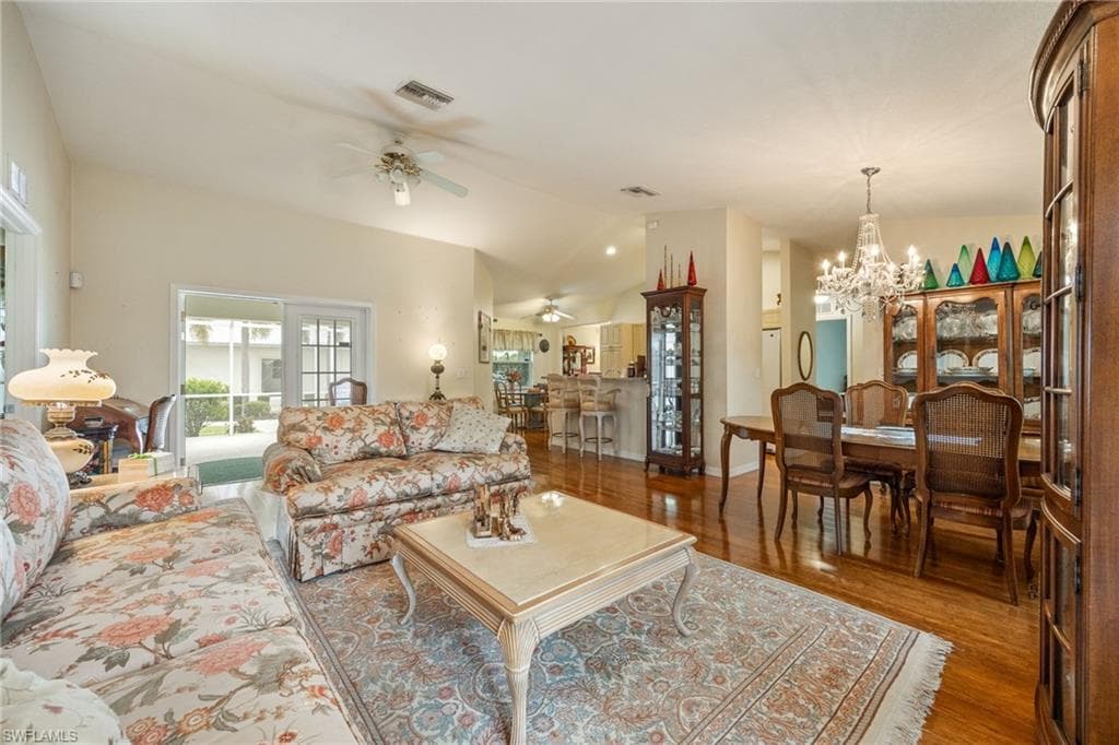 Living room featuring vaulted ceiling, wood finished floors, a chandelier, and ceiling fan