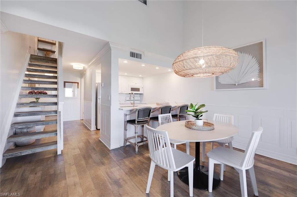 Dining area with wainscoting, a decorative wall, stairway, dark wood-style floors, and a towering ceiling