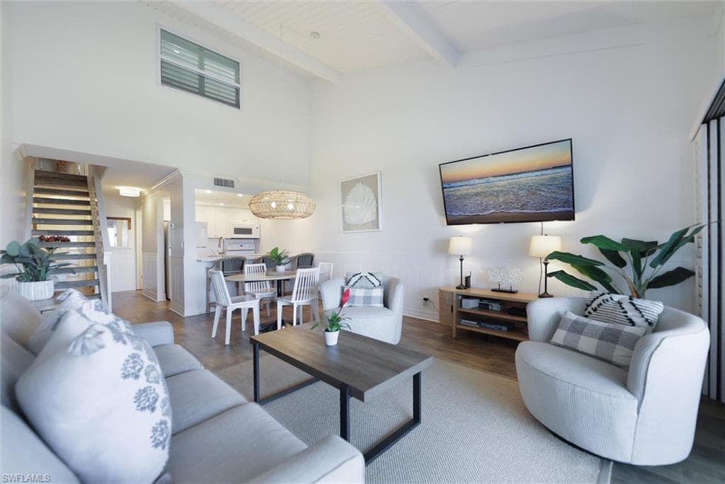 Living area with wainscoting, wood finished floors, beamed ceiling, stairs, and a decorative wall