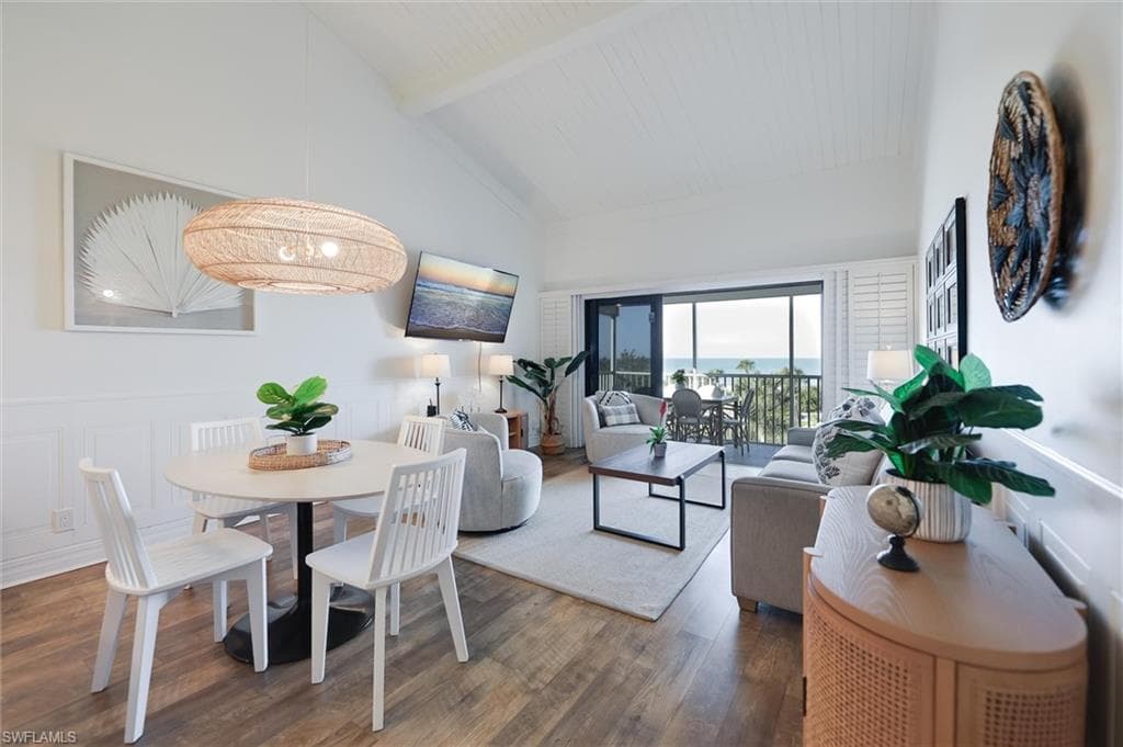 Dining space with a decorative wall, beamed ceiling, wood finished floors, wainscoting, and high vaulted ceiling