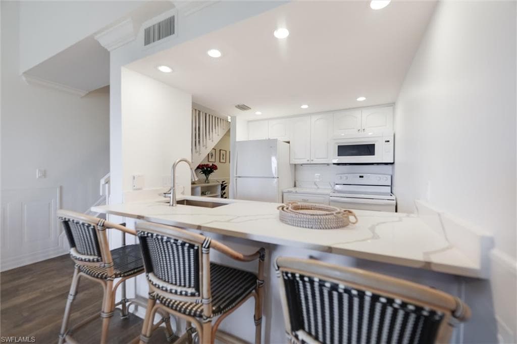 Kitchen with white cabinetry, white appliances, a breakfast bar area, recessed lighting, and a peninsula