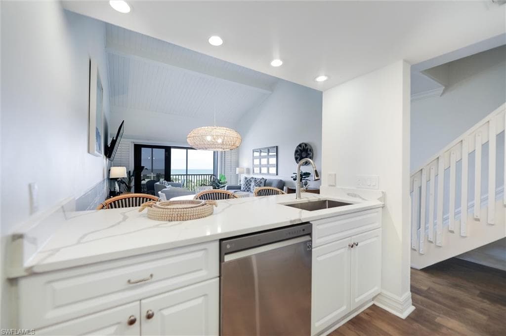 Kitchen featuring stainless steel dishwasher, light stone counters, white cabinets, vaulted ceiling, and dark wood-style flooring