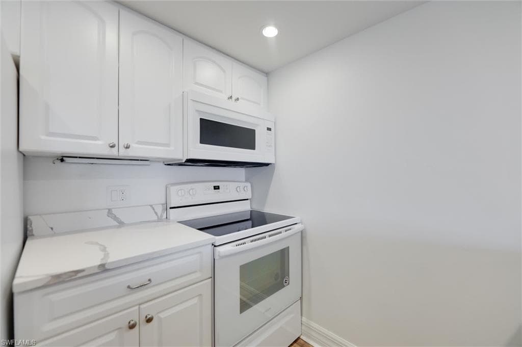Kitchen with white appliances, white cabinets, recessed lighting, and light stone counters
