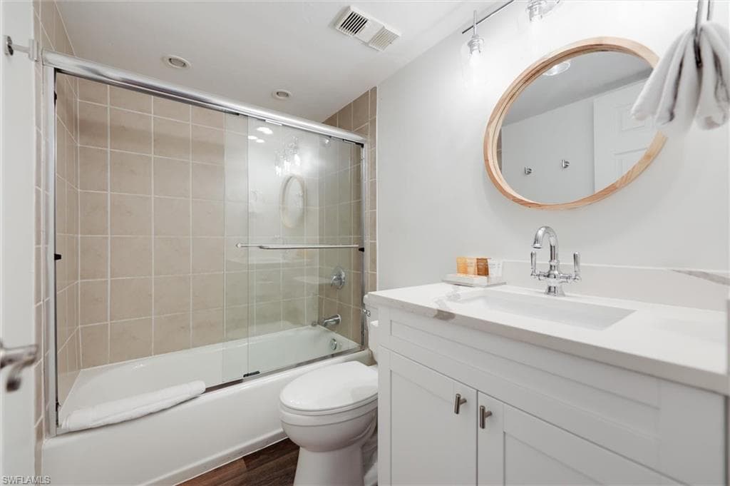 Full bathroom with vanity, shower / bath combination with glass door, and dark wood-style floors