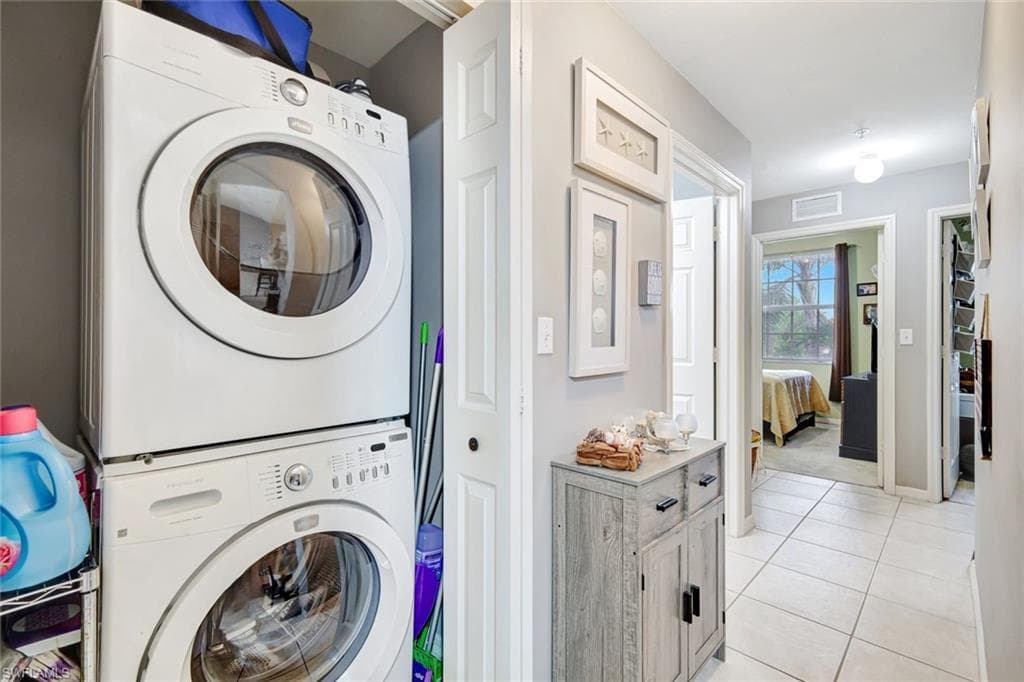 Laundry room with stacked washing machine and dryer and light tile patterned floors