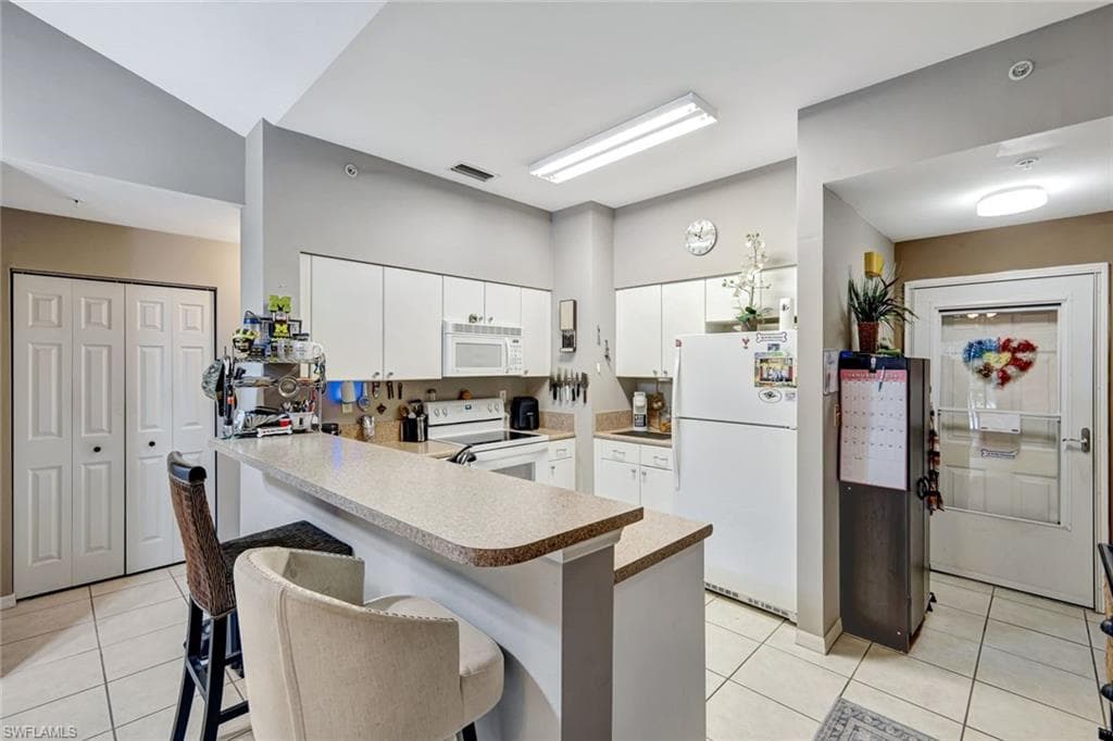 Kitchen featuring white appliances, light tile patterned floors, a kitchen bar, and a peninsula