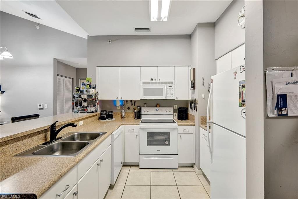 Kitchen with white appliances, white cabinetry, light countertops, and a peninsula