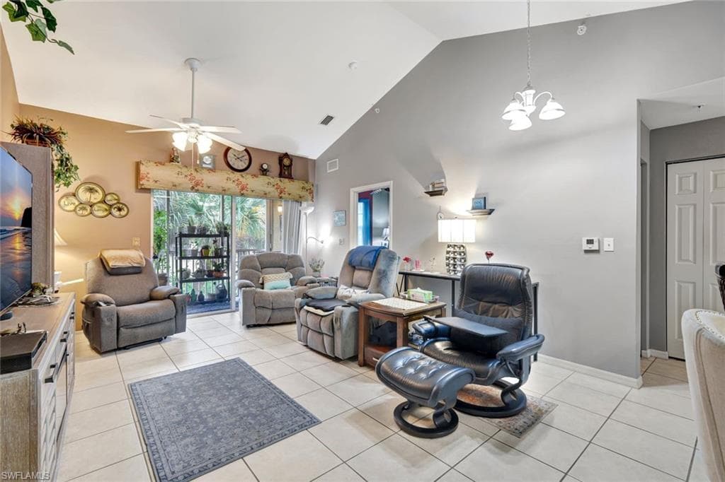 Living area with light tile patterned floors, high vaulted ceiling, ceiling fan, and a chandelier